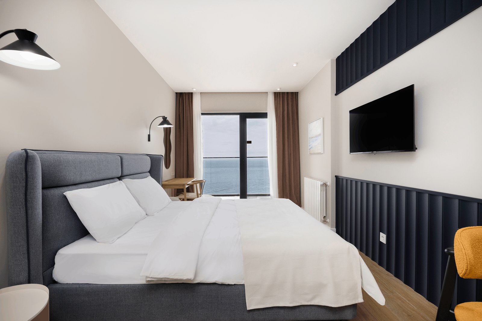 Furnished bedroom at NEXT White with a grey upholstered bed and balcony doors